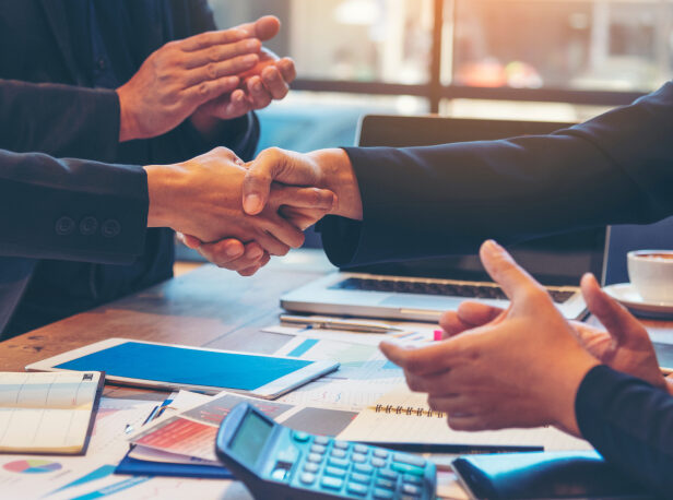 Four business people sitting at a table with two of them shaking hands.